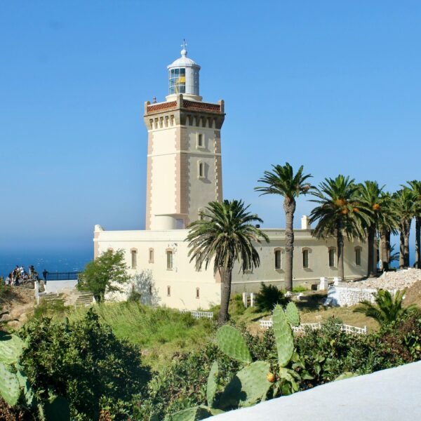 A scenic view of Cape Spartel Lighthouse surrounded by lush palm trees on a sunny day in Morocco.