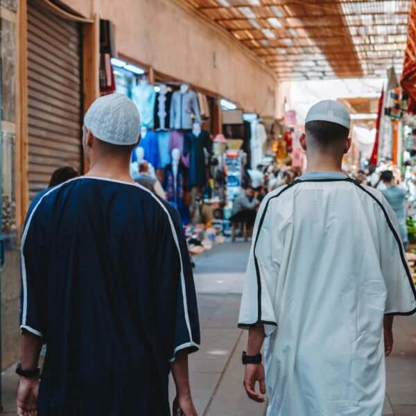 Men walking through Marrakesh's bustling market with vibrant stalls and traditional attire.