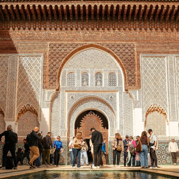 Group of tourists exploring Ben Youssef Madrasa's intricate architecture in sunny Marrakech.