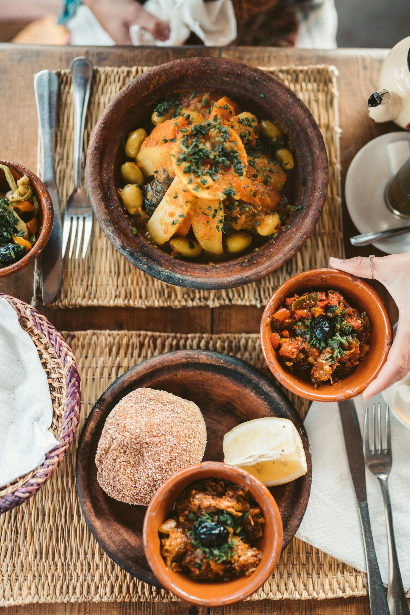 Delicious Moroccan dishes served with fresh vegetables and traditional bread on a woven mat.